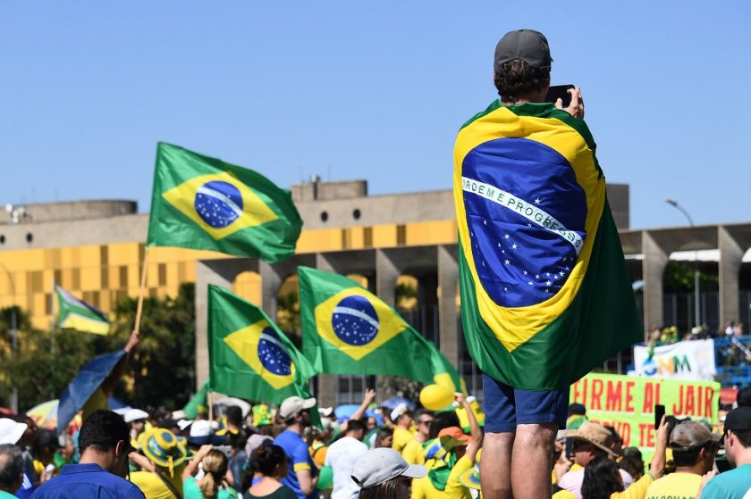 A supporter of Brazilian President Jair Bolsonaro wrapped in a Brazilian flag takes part in a demonstration in front of the National Congress in Brasilia to shore up the ultraconservative government as it faces growing opposition, while marches are planned across Brazil on May 26, 2019. - Bolsonaro, who took power in January on a promise to revive Latin America's biggest economy, has seen his popularity plunge as rising unemployment and education spending freezes fuel opposition to his administration, which is plagued by infighting. (Photo by EVARISTO SA / AFP)